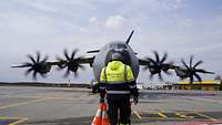 Ein Einweiser des Bodenpersonals steht mittig vor einem A400M.