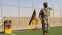 Ein Soldat steht in militärischer Grundstellung. Hinter ihm befinden sich die Deutschlandflagge und ein Rednerpult