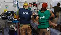 Ärztin und ein Pfleger stehen um ein Patientenbett auf dem eine Soldatin liegt