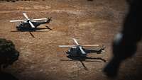 Zwei Hubschrauber sind kurz davor, von einem sandigen Feld abzuheben.