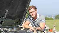 A man looking inside the engine compartment of a vehicle