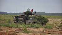 Ein Schützenpanzer Marder steht auf sandigem Boden im Gelände