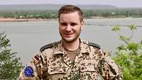 Ein Soldat steht vor dem Fluss Niger und lächelt in die Kamera