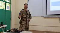 Ein Soldat steht in einem Hörsaal und hält einen Vortrag mithilfe einer PowerPoint-Präsentation