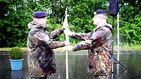 Zwei Soldaten stehen sich gegenüber, einer übergibt dem anderen einen Kompaniewimpel.