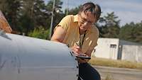 A woman taking notes while kneeling in front of a metal pipe.