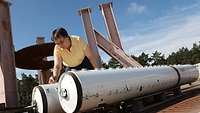 A woman bending over two long containers