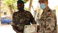 Ein malischer Soldat steht neben einem deutschen Soldat und hält sein Zertifikat in der Hand