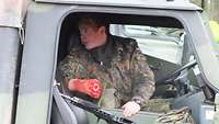 Ein Soldat sitzt in einem Gefechtsfahrzeug mit einem aufgesetzten, künstlichen, blutigen Armstumpf.