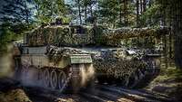 Ein Kampfpanzer Leopard fährt über einen Waldweg. Ein Soldat schaut aus der Luke