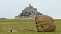 Auf einer Wiese vor der Inselburg Mont Saint-Michel landet ein Soldat mit Fallschirm.