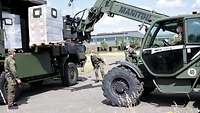 Soldaten mit Mund-Nasenschutz entladen eine Palette Verpflegungsrationen mit einem Manitou-Teleskopstapler