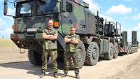 Zwei Soldaten stehen vor einem großen grün-braun- schwarzen Lastkraftwagen mit Sattelauflieger