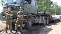 Zwei norwegische Soldaten stehen mit verschränkten Armen vor ihrem Lastkraftwagen und lächeln in die Kamera