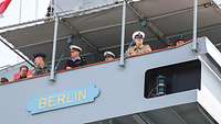 Marinesoldaten in unterschiedlichen Uniformen schauen von einem grauen Schiff.