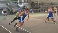 Ein Spieler dribbelt an seinem Gegenspieler vorbei, vor ihm versperrt ein weiterer Mitspieler den Laufweg zur Verteidigung.