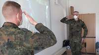 Zwei Soldaten stehen sich in einem Unterrichtsraum gegenüber und halten zum militärischen Gruß die rechte Hand an die Schläfe