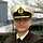 Portrait Prof. Dr. Brülls Ein Mann steht in Marine-Uniform in einer parkähnlich angelegten Anlage, im Hintergrund ein großes altes Gebäude