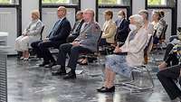 Mehrere Personen sitzen auf Stühlen in einem Saal