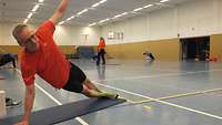 Ein Mann stützt seinen gestreckten Körper mit seitlich ausgestrecktem Arm vom Boden ab und hält die Ballance
