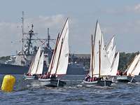 Kieler Woche Vier kleine graue Boote segeln auf offenem Wasser, im Hintergrund ein graues Kriegsschiff.