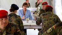Eine Frau in hellblauem Kostüm spricht mit zwei Soldatinnen und einem Soldaten an einem Tisch sitzend.