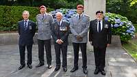 Drei Veteranen der britischen Streitkräfte stehen mit zwei Bundeswehrsoldaten vor einem Gedenkstein.