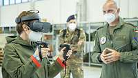 Eine Zivilistin trägt eine Virtual-Reality-Brille und hält zwei Controller in den Händen. Ein Soldat steht erklärend daneben.