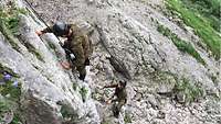 Zwei Soldaten der Gebirgsjägertruppe klettern ohne Waffen und Ausrüstung eine Felswand hinauf.