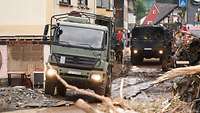 Zwei Bundeswehr-LKW durchqueren einen vom Hochwasser zerstörten Stadtteil von Bitburg.
