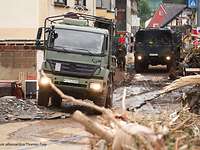 Zwei Bundeswehr-LKW durchqueren einen vom Hochwasser zerstörten Stadtteil von Bitburg.