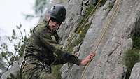 Ein Soldat steht angeseilt an einer Felswand und schaut nach unten.