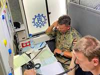 Ein Soldat und ein Mitarbeiter des technischen Hilfswerks telefonieren in einer Kabine.