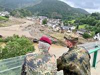 Zwei Soldaten schauen von einer Brücke auf ein vom Hochwasser zerstörtes Dorf