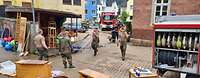 Mehrere Soldaten und Feuerwehrleute stehen auf einem Platz. Es stehen Gegenstände herum, die nach dem Hochwasser gerettet wurden