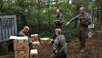 Soldaten hocken und stehen im Wald neben Munitionskisten.
