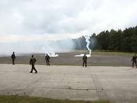 Soldaten stehen auf einer Freifläche, wo Nebel und kleine Flammen von gerade explodierten Nebelhandgranaten zu sehen sind.