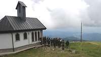 Neben einer Kapelle steht eine Gruppe Soldaten und blickt ins Tal.