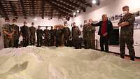 Mehrere Soldaten stehen in einem Museum um ein Geländemodell herum, unter ihnen ein Zivilist, der redet.