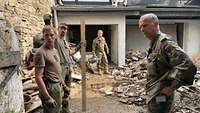 Soldaten stehen in einem Hinterhof voller Schutt. Einer berichtet einem General von der Arbeit