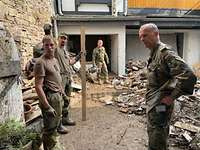 Soldaten stehen in einem Hinterhof voller Schutt. Einer berichtet einem General von der Arbeit