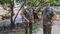 Zwei Soldaten stehen vor Schutt und Geröll an einem Fluss