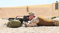Ein Soldat liegt auf dem Boden. Die Waffe ist auf einem Rucksack aufgelegt und der Soldat sieht durch das Zielfernrohr