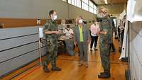 Die Wehrbeauftragte hinter einer Impfkabine im Gespräch mit einer militärischen Ärztin und einem Soldaten.