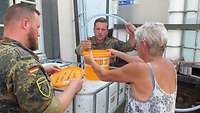 Zwei Soldaten pumpen Wasser aus einem Kanister in den Eimer einer Frau