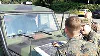 Drei Soldaten besprechen den Einsatz, vor ihnen eine Karte auf der Motorhaube ihres Fahrzeugs