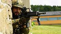 Ein Soldat der angelehnt an eine Wand das Gewehr hält.