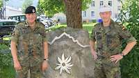 Zwei Soldaten stehen vor einem Felsstein mit einem Schriftzug und Edelweiß darauf.