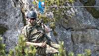 Ein Soldat hängt mit einem Tragegeschirr an einem Seil zwischen zwei Felsen.