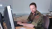 Ein Soldat sitzt vor einem Computer am Schreibtisch am blickt auf den Bildschirm